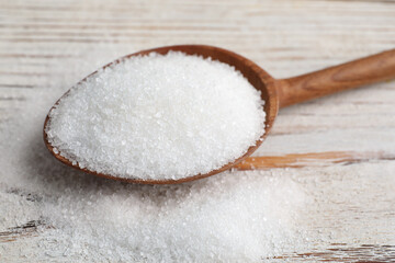 Fototapeta na wymiar Spoon with granulated sugar on white wooden table, closeup