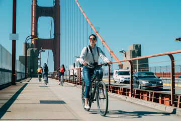 full length asian woman is enjoying cityscape while cycling at leisure on golden gate bridge in San...