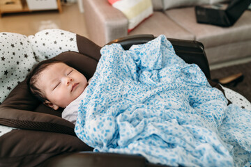 adorable asian new baby covered with blanket is sleeping alone peacefully in the nursery glider...