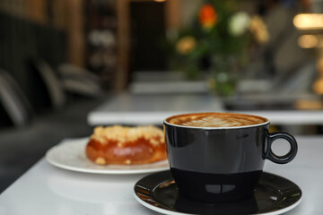 Cup of fresh coffee and bun on table in cafeteria