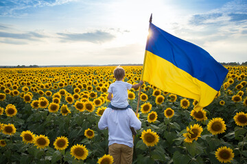 dad with son, who sits on shoulders, with large flag of Ukraine against backdrop of flowering field...