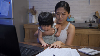 asian mother holding her toddler child is worrying about the over budget family expenditure while...