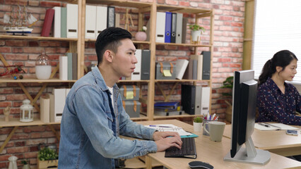 focused asian engineer is writing down data on his notebook with hand under chin while developing a...