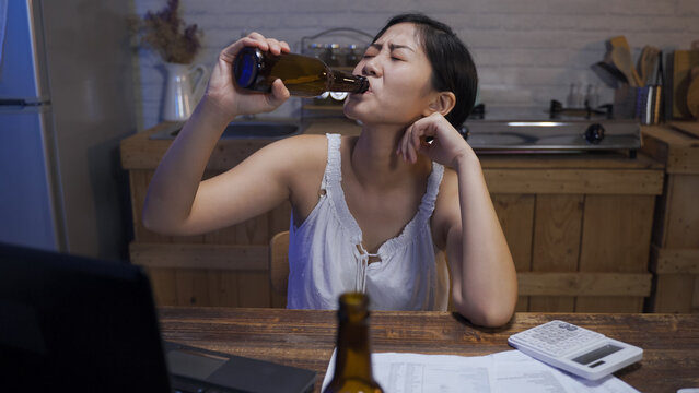 Asian Young Woman Propping On The Dining Table Drinking Beer Alone Is Looking Into Distance While Thinking About Her Financial Problems.