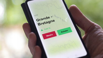 Un investisseur analyse un fonds etf grande - bretagne sur un graphique. Un téléphone affiche le cours de l'ETF. Texte en français francais Grande - Bretagne