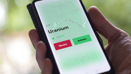 Un investisseur analyse un fonds etf uranium sur un graphique. Un téléphone affiche le cours de l'ETF ressource nucléaire. Texte en français francais.  © maurice norbert