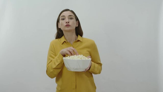 Character portrait of young woman greedily eating popcorn while watching an exciting movie. Young woman eating potato chips, snacks or popcorn on white background.
