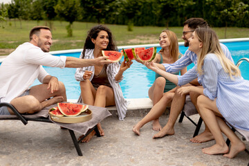 Young people sitting by the swimming pool and eating watermelon in the house backyard