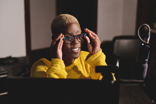 Positive Black Female Broadcaster With Short Hair Adjusting Glasses And Looking Away During Work In Contemporary Radio Studio