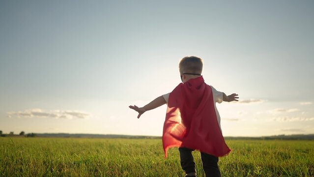 superhero. little boy running across the field in a superhero costume with a red cape silhouette at sunset. happy family kid dream concept. baby superhero. little boy in sunset run through