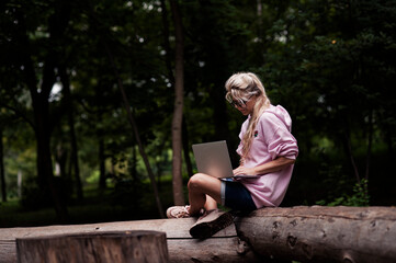 A girl with a laptop works while walking in the park in a cozy place, enjoys it. Online learning, freelancing and fun concept, talk by mobile cell phone look aside. People urban lifestyle concept