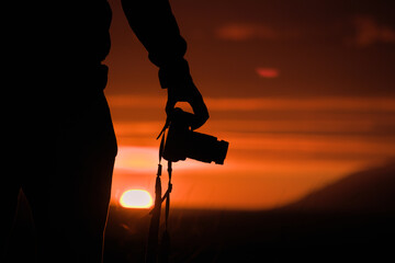 Silhouette eines jungen Fotografen bei Sonnenuntergang und Sonnenaufgang in Island am Meer mit...