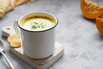 Squash or pumpkin vegan soup in metal mug. A cup of creammy autumn soup gray background with pumpkin slices.