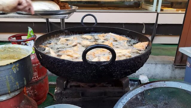 An Indian street vendor prepares snacks Samosas frying in oil at Ramadhan market in India. Making Of Delicious And Crunchy Samosas. Closeup Of Bubbles In Oil In Making Of Samosas. deep frying samosa