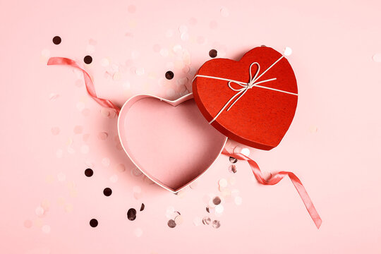 Top view of an open empty red heart shaped box on pink confetti background for your products.