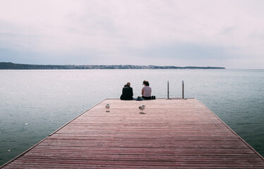 Couple man and woman sitting on sea coast dock watching the horizon - 520994699