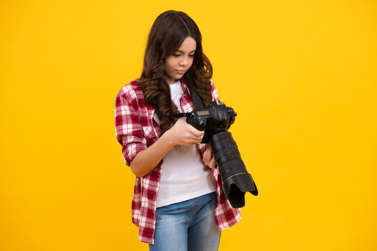 12, 13, 14 year old teen girl holding digital camera or DSLR over yellow background.