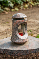 Fototapeta premium Grave light with burning candle on a grave with flowers