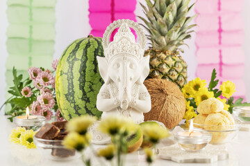Sculpture of Lord Ganesha with offerings, fruits, sweets, flowers and candles on a light background with decorations. Holiday of Ganesh Chaturthi. Ganesh festival. Hindu religion holidays