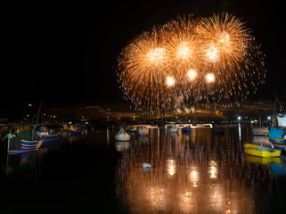 Marsaxlokk,Malta-Fireworks show,colorful fireworks on the black sky background with some boats under them during religion feast in Marsaxlokk fishing village. Yellow fireworks. Maltese feast