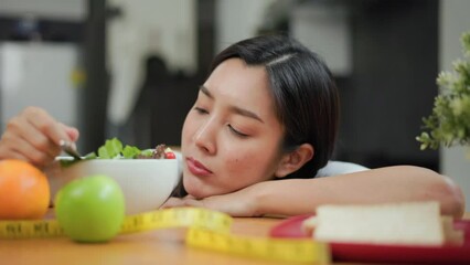 Unhappy female looking to organic greens vegetable salad in weight loss diet and wellness on table. Tired woman dislike eat bored with food healthy salad breakfast in kitchen. Diet food concept.