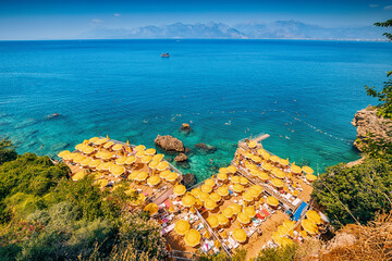Aerial view of hidden narrow and cozy beach among cliffs and rocks with bright yellow umbrellas and...