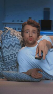 vertical video of young man using remote controller while watching tv on couch