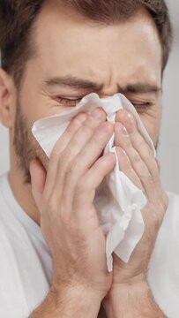 vertical video of bearded man sneezing in tissue and using nasal spray at home