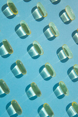 Fish oil pills pattern on a pastel blue background. Flat lay creative design. Omega D3 vitamin.