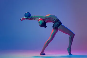 Foto op Plexiglas Portrait of young girl, rhythmic gymnast athlete performing with blue ball isolated on blue purple background in neon light © Lustre