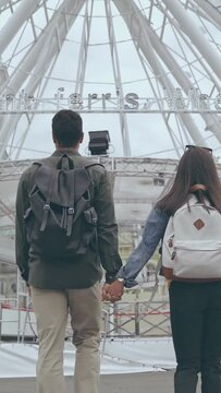 vertical video of back view of couple with backpacks walking to ferris wheel
