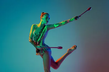 Foto op Plexiglas Portrait of young tender girl, female rhythmic gymnast performing with clubs isolated over gradient blue background in neon light © Lustre