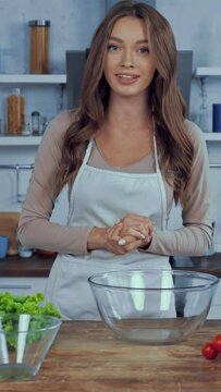 vertical video of happy woman in apron talking and pointing with hands at ingredients on table