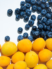 A group of fresh appetizing apricots and blueberries lie on a white background in daylight, close-up of the fruit