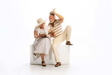 Emotional senior man and woman in her 60's in vintage attire sitting together isolated on white...