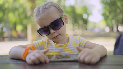 Little girl in mom's sunglasses is learning foreign language by repeating words from mobile phone....