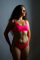 Obraz premium a beautiful Brazilian woman in a pink swimsuit poses on a gray background