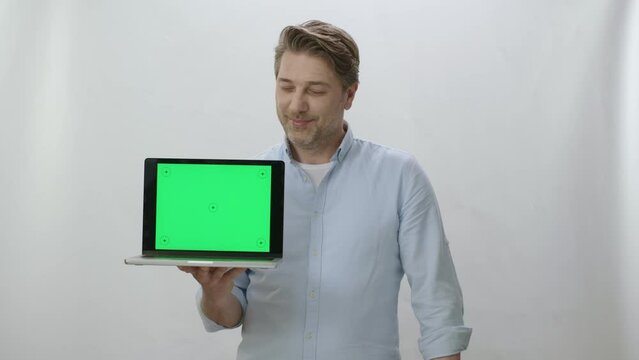 Portrait of happy businessman holding laptop with green screen. Happy businessman working on white background showing everything is perfect. You can put anything you want inside the computer.