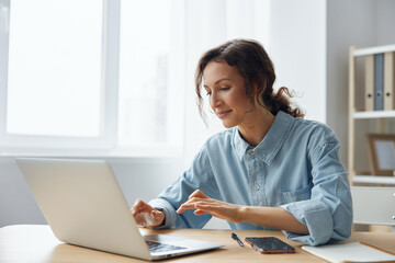 Cheerful adorable curly businesswoman worker freelancer chatting with client registers an order in social media in light office. Happy employee work on computer online in support service. Copy space