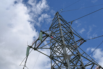 Looking up steel power pylon construction with high voltage cables against blue sky.