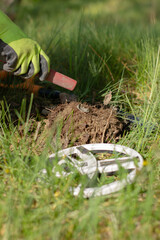 vertical photo a hand in a glove using a pinpointer looks for a treasure in the dug-out earth, but found rubbish. in the foreground in blur is the coil of a wireless metal detector. In the background