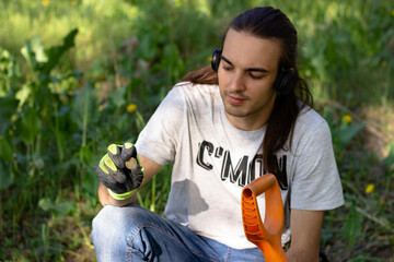 a young man holds a coin - garbage found using a wireless metal detector and a pinpointer in the park. grass in the background
