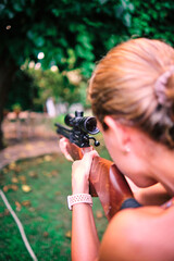 Left-handed woman practicing target shooting with an airgun in her garden.