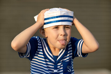 A boy of 7-8 years old in a sailor suit teases and shows his tongue. Close-up portrait of a child.