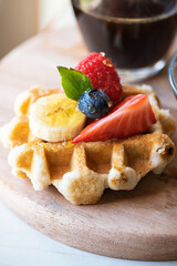 Close up of waffles with berries and honey on a wooden board.