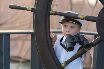 The boy is the captain of the ship. A boy in the form of a ship captain listens to a sea shell. Dream about the sea. Future captain. Model of a ship in the park