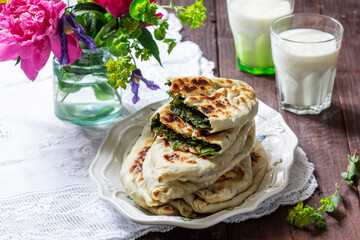 Traditional Armenian flatbread with greens zhengyalov hats, served with yogurt on the background of a bouquet.