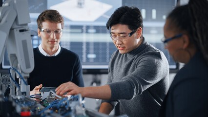 Male Student Holding a Tablet And Pointing at Robotic Hand While Working on Project with Asian...