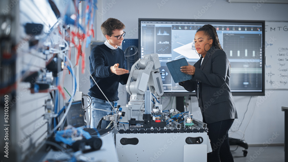 Poster black teacher holding tablet and discussing robot hand with caucasian student during the lesson at s