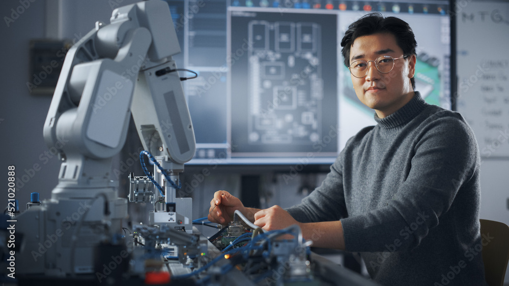 Poster Asian Male Engineer Sitting at Table And Looking at Camera While Woking on New Engineering Project. Robot is Moving Under his Control. Education and Robotics In Modern University Concept.